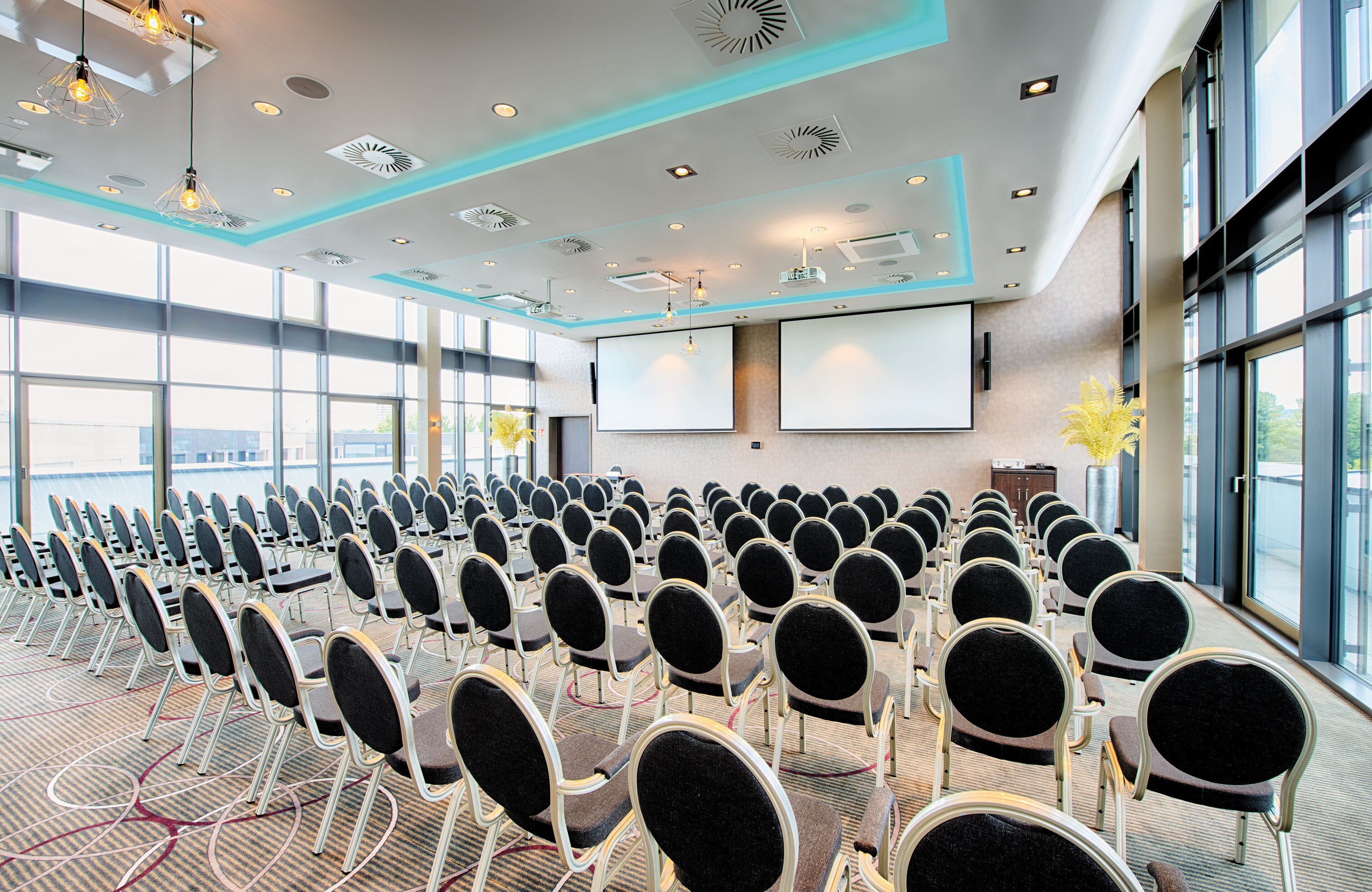 A conference room with rows of chairs, a large screen, and a projector.