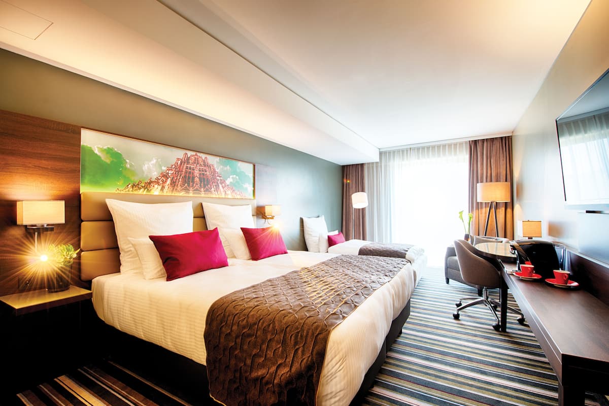 A hotel room with a large bed, a desk, a chair, and a painting on the wall.
