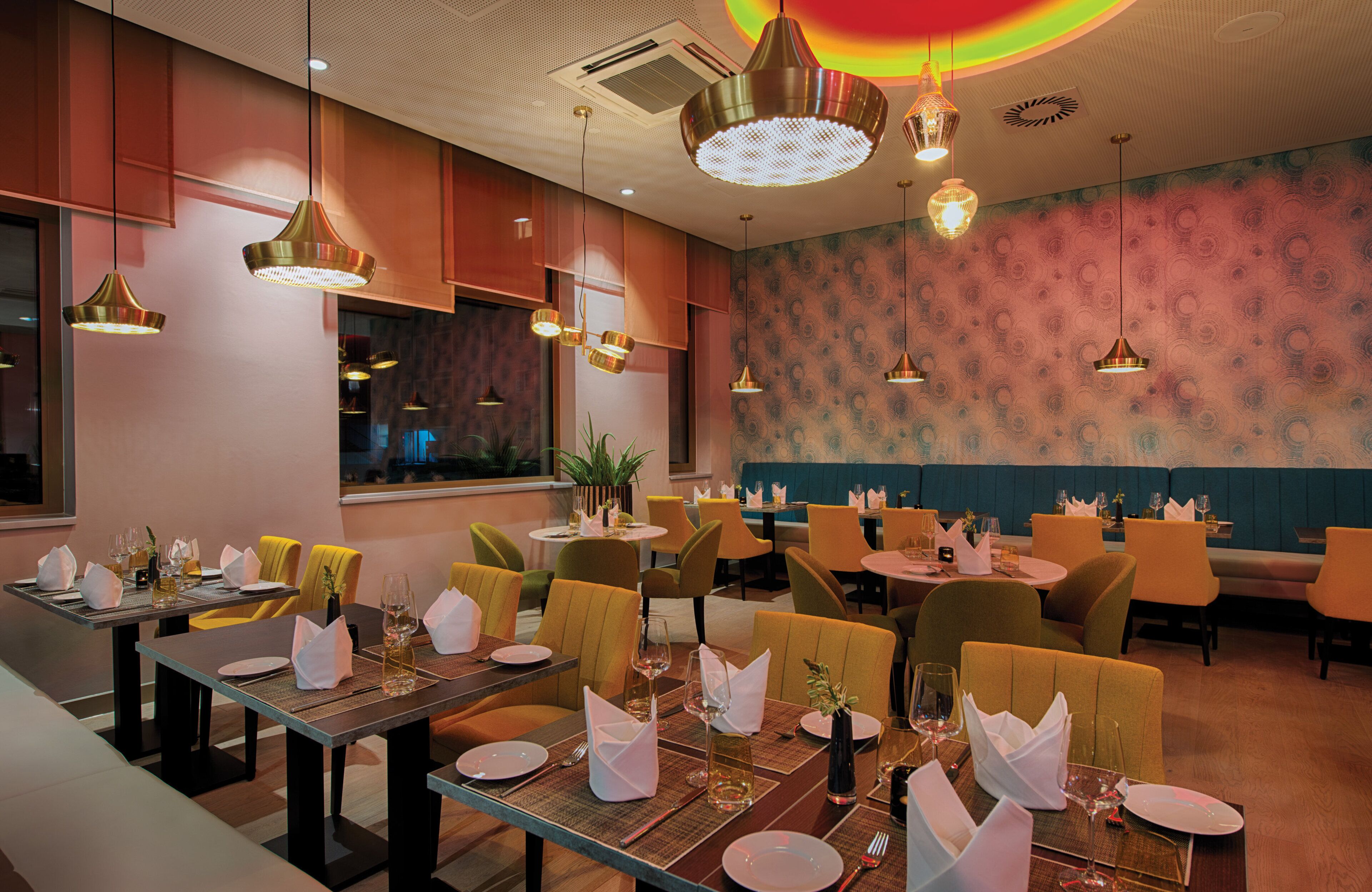 Ein Restaurantinneres mit mehreren Speisetischen, Stühlen und hängenden Pendelleuchten.