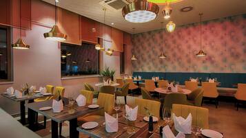 Ein Restaurantinneres mit mehreren Speisetischen, Stühlen und hängenden Pendelleuchten.