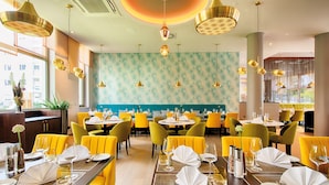 Un restaurante con sillas amarillas, mesas redondas y una pared azul turquesa estampada.