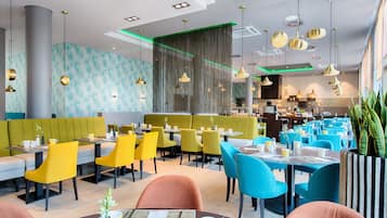 Ein modernes Restaurant mit Sitzboxen und Tischen, Polsterungen in Grün- und Gelbtönen und Pendelleuchten.