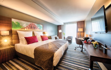 A hotel room with a large bed, a desk, a chair, a TV, and a painting on the wall.