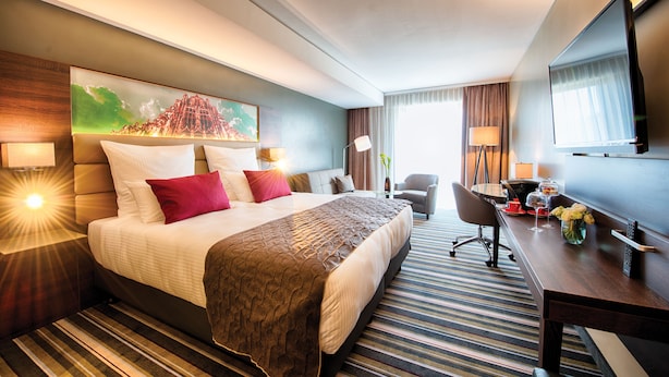A hotel room with a large bed, a desk, a chair, a TV, and a painting on the wall. - Leonardo Royal Hotel Ulm (Ulm)