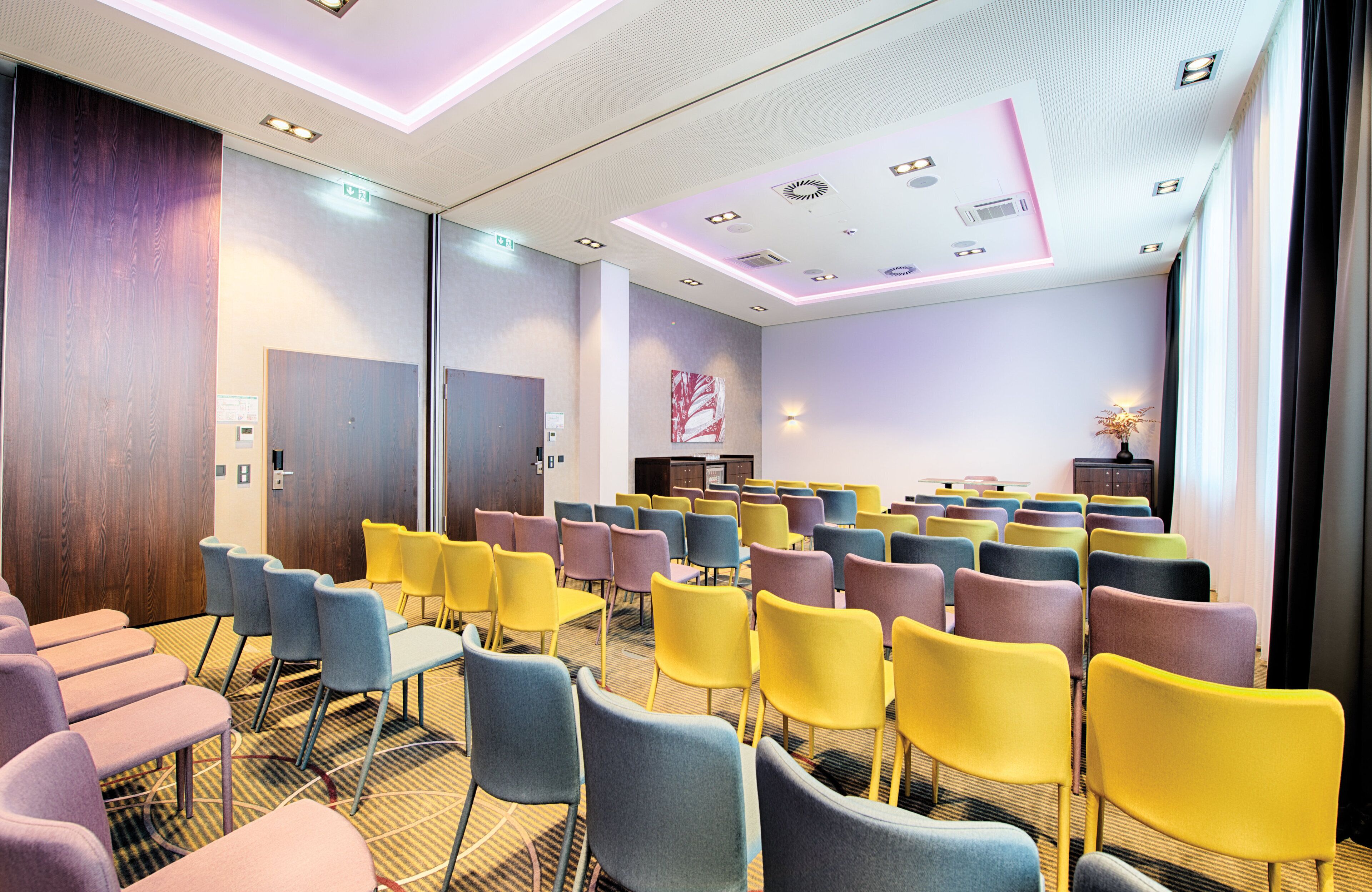 A conference room with rows of chairs, a stage, and a large window.