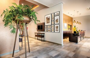 A modern interior with a reception desk, framed photographs on the wall, and a large potted plant.