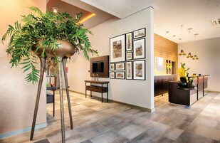 Un interior moderno con una mesa de recepción, fotografías enmarcadas en la pared y una planta grande en maceta.