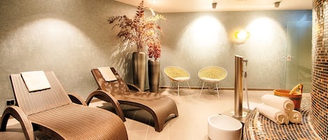 Un área de spa con sillones de mimbre, una camilla de masaje, una mesita con toallas y un calentador fijado a la pared.