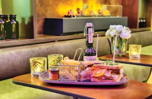 Una mesa con un sándwich, una botella de vino y vasos decorativos.