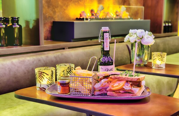 A table with a sandwich, a bottle of wine, and decorative glassware. - Leonardo Royal Hotel Ulm (Ulm)