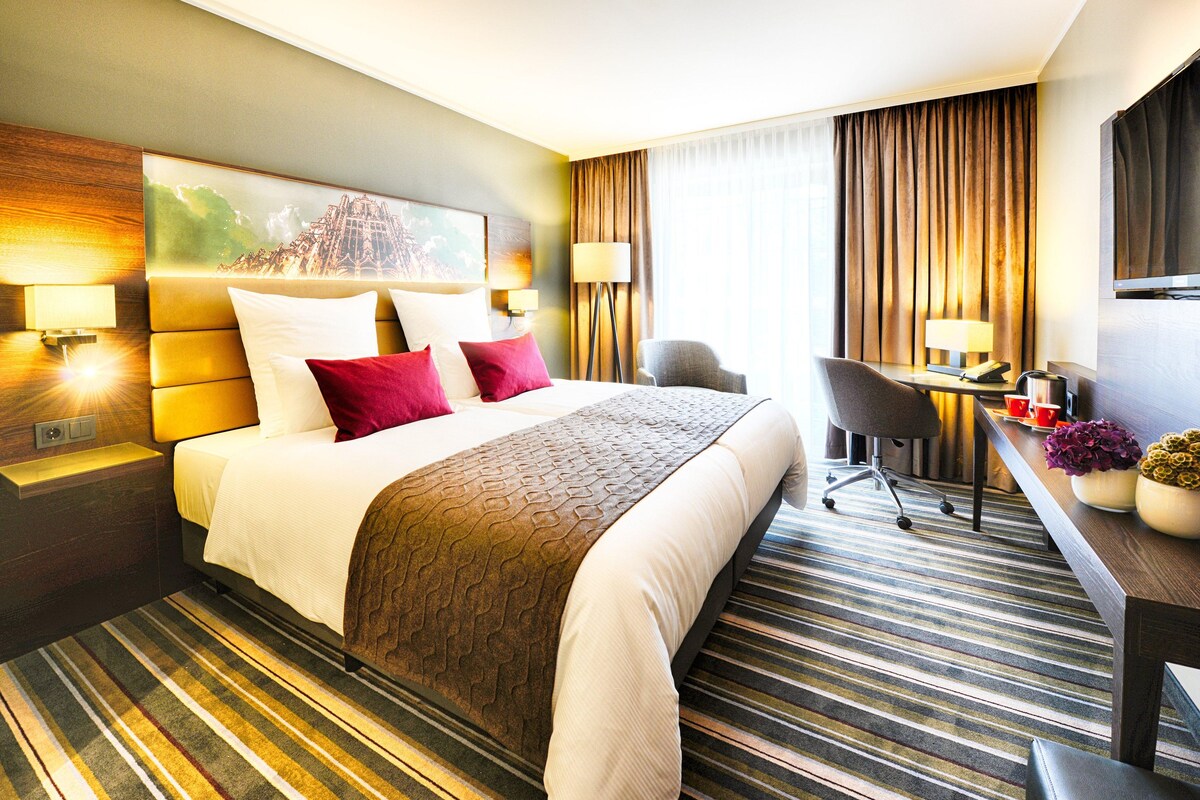A hotel room with a large bed, a desk, a chair, and a television.