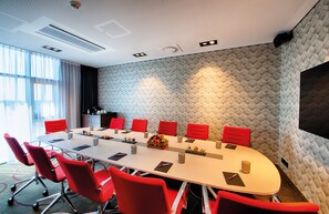 A conference room with a long table, red chairs, and a geometric patterned wall. - Leonardo Royal Hotel Ulm (Ulm)