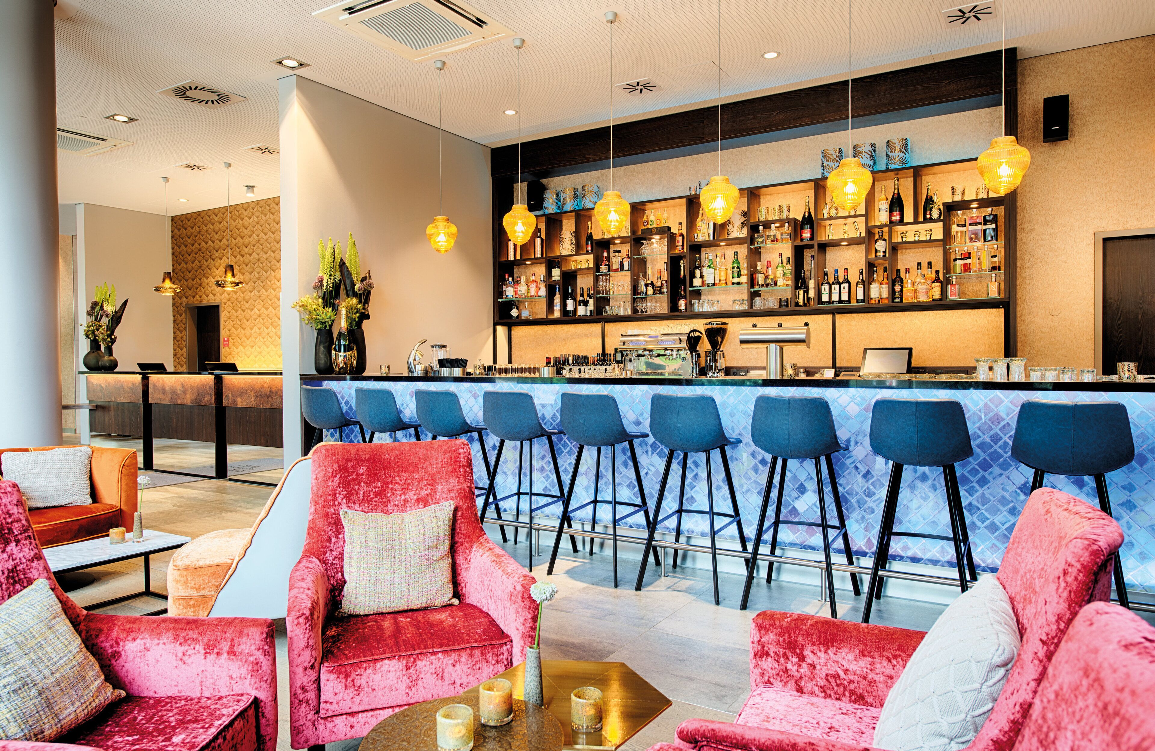 A bar area with a counter, bar stools, and a seating area with red velvet chairs.
