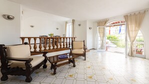 A living room with a wooden sofa set, a dining table with chairs, and a view through an open door to a balcony. - Hotel Antonella (Ischia)