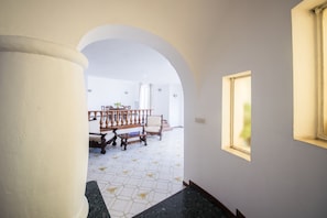 Um corredor com piso de azulejos, um banco de madeira e uma mesa com cadeiras.