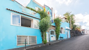 A blue building with a balcony, a window with a curtain, and a door. - Hotel Antonella (Ischia)
