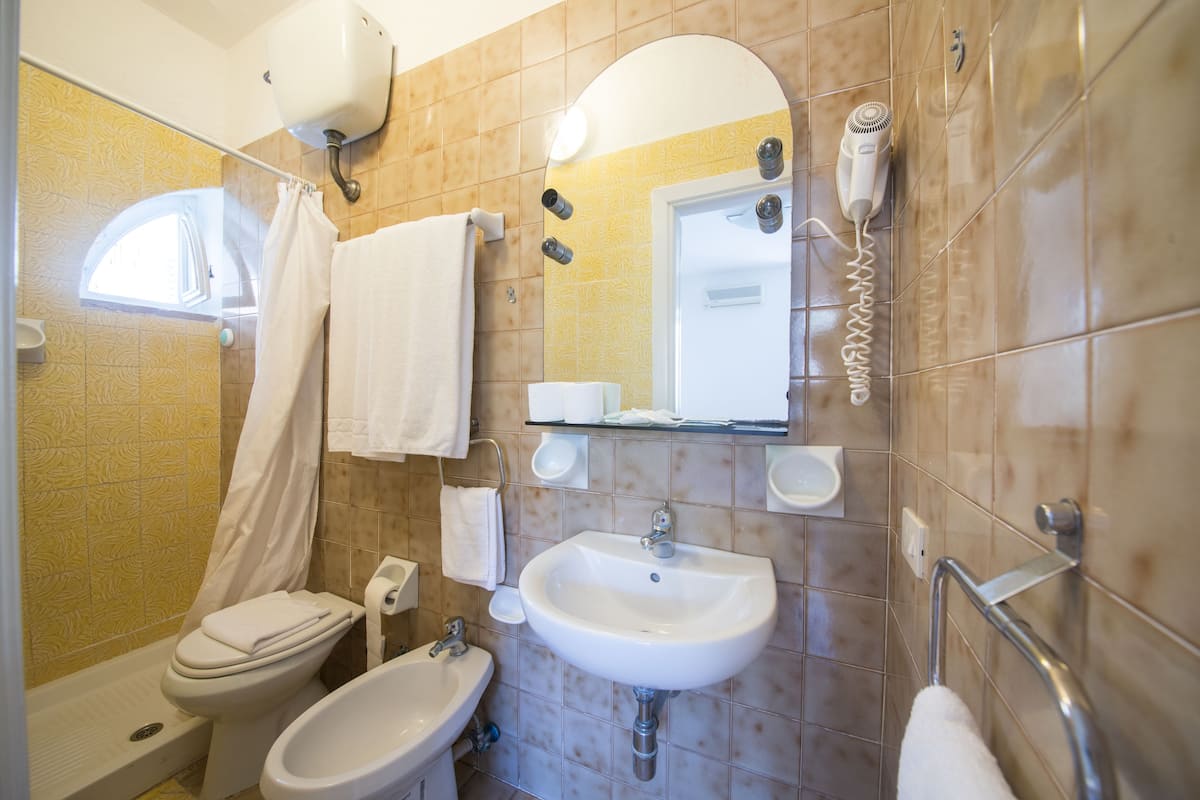 A bathroom with a toilet, bidet, sink, and a hairdryer mounted on the wall.