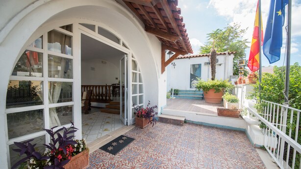 A covered outdoor area with a tiled floor, a wooden pergola, and potted plants. - Hotel Antonella (Ischia)