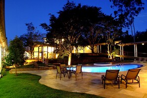 An outdoor pool area with a table and chairs, surrounded by a well-maintained lawn and trees. - Pousada Boutique Oratorio (Tiradentes)