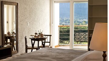 Un dormitorio con un ventanal grande, un balcón con vistas al campo, una mesa de comedor con juego de té y un espejo en la pared.