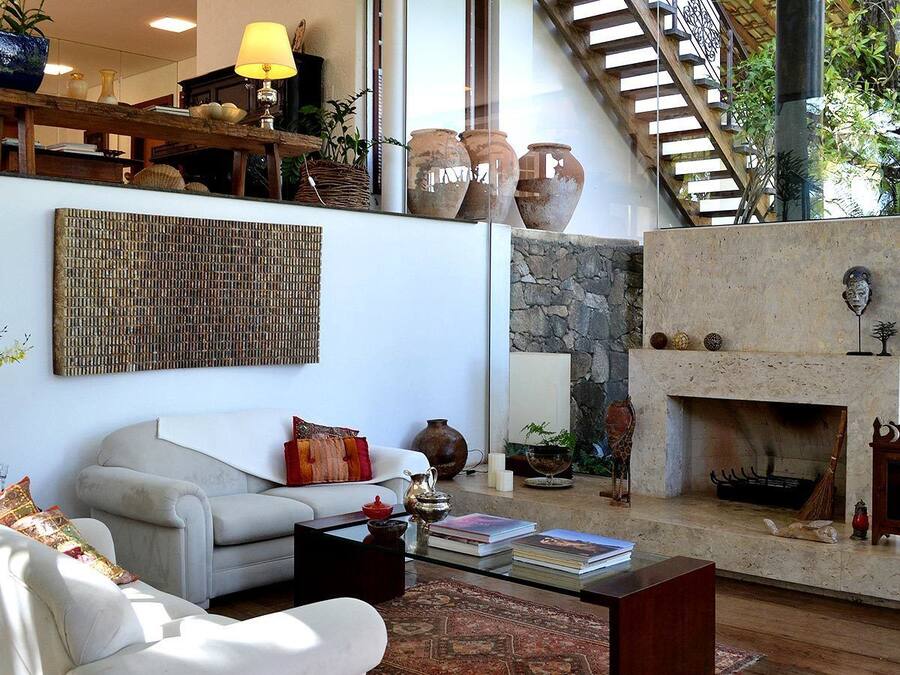 A spacious living room with a white sofa, a coffee table with books, a fireplace, and a staircase leading to an upper level.