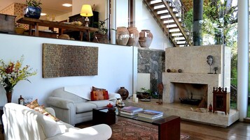 Amplia sala de estar con un sofá blanco, una mesa de centro con libros, una chimenea y una escalera que sube a un nivel superior.