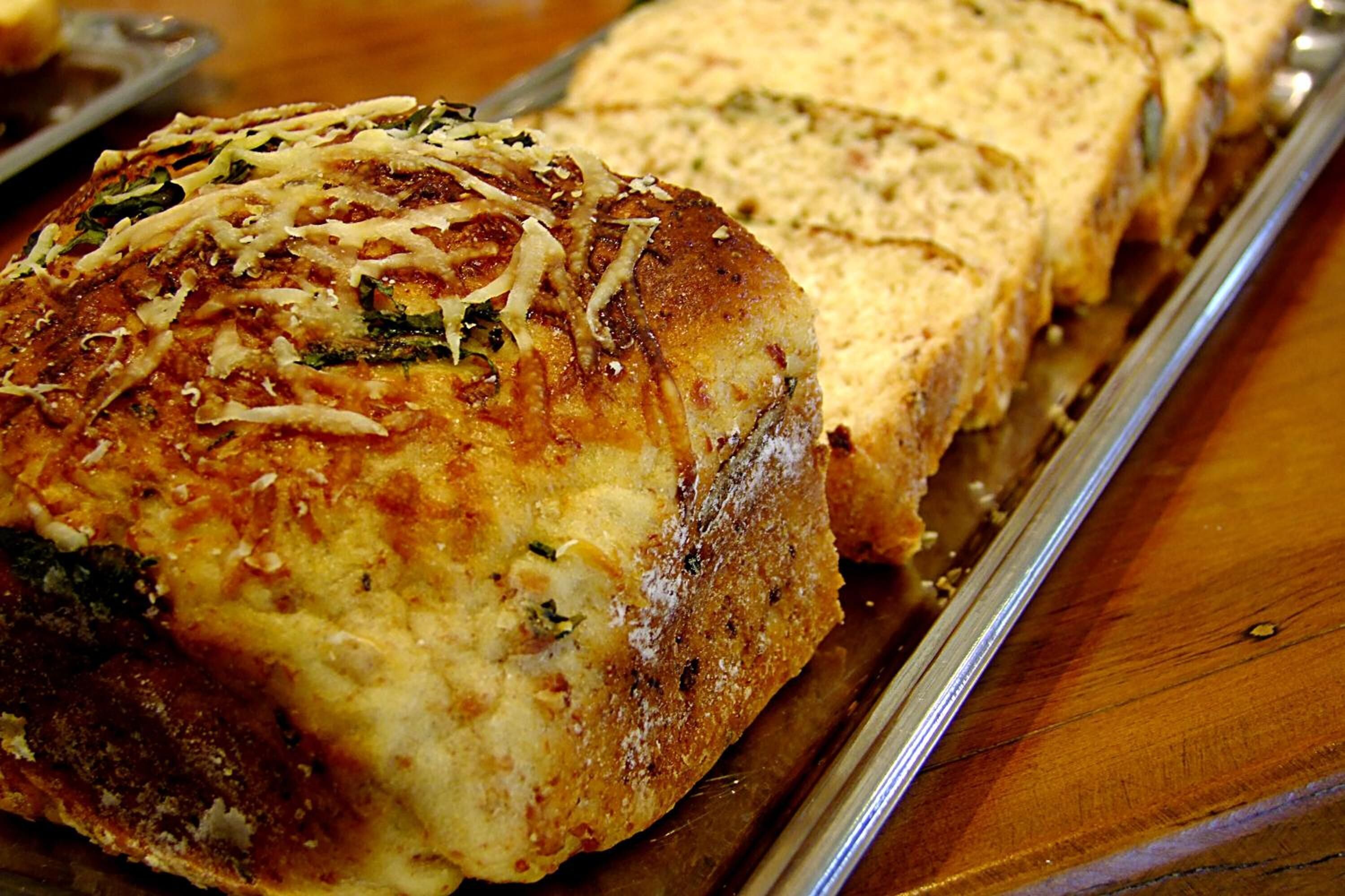 Une miche de pain garnie de fromage et d’herbes, posée sur une surface en bois.