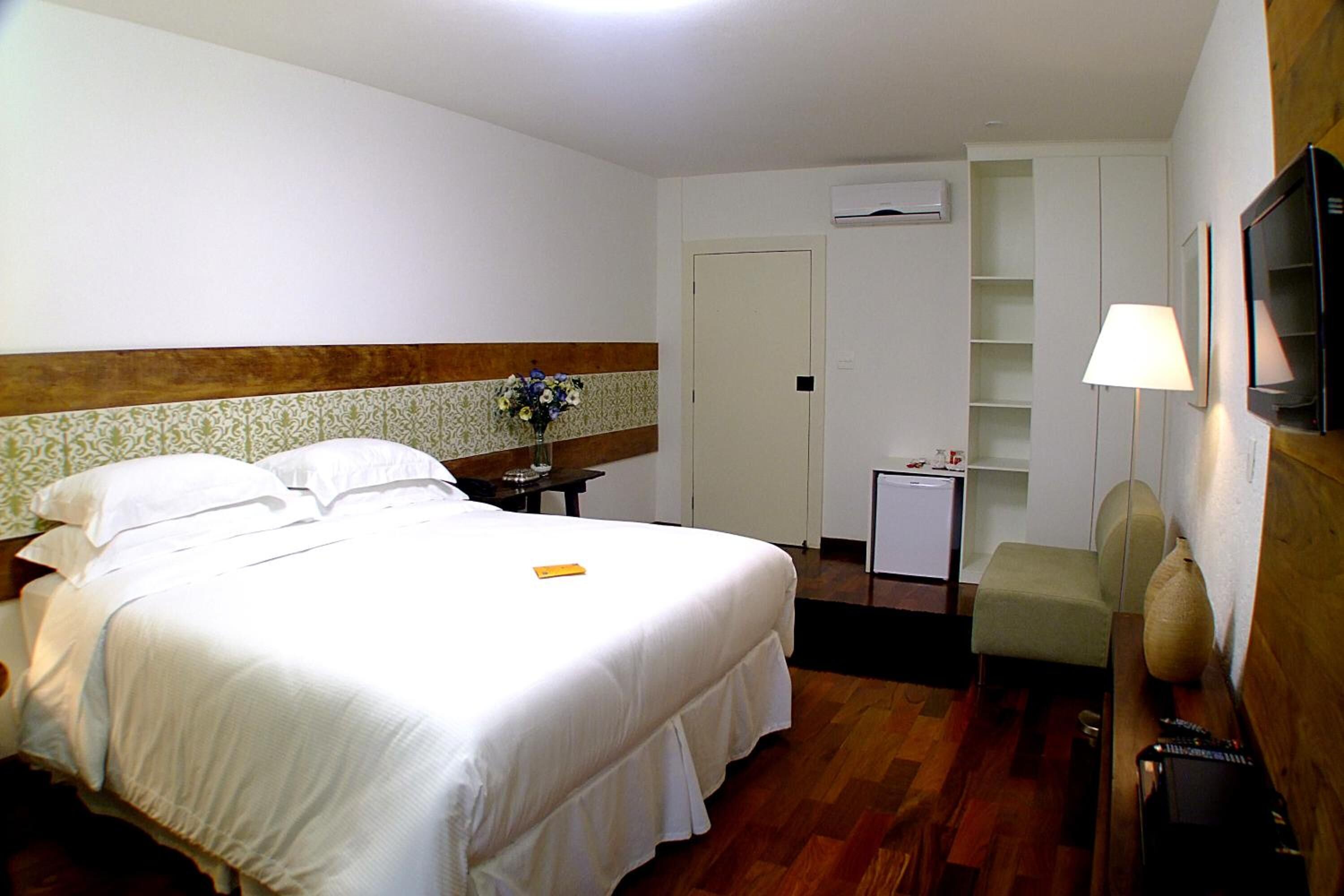 A hotel room with a large bed, a desk, a chair, a TV, and a small table with a vase of flowers.