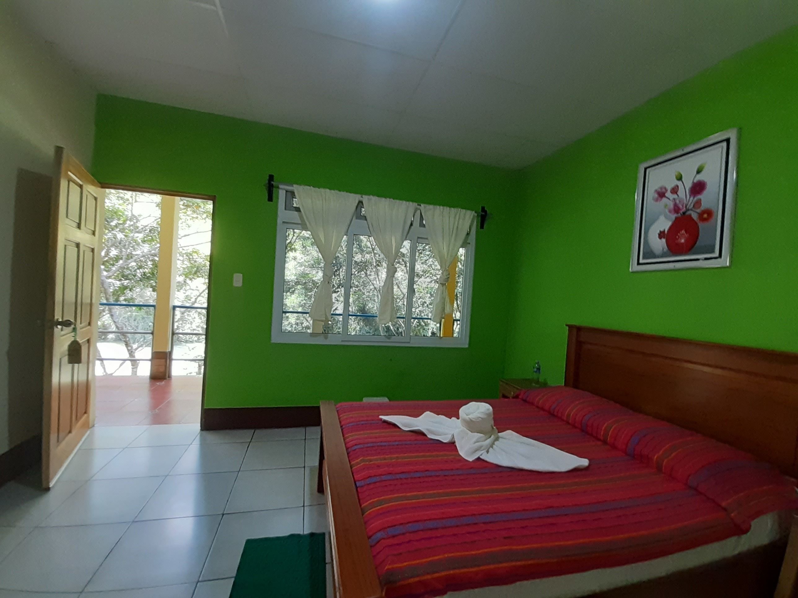 A room with green walls, a bed with a striped red blanket, a window with white curtains, and a door leading outside.