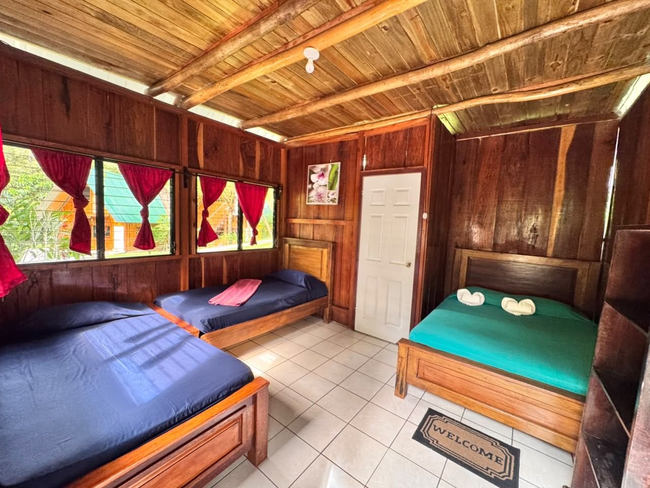A room with two single beds, a wooden ceiling, a door, and a welcome mat.