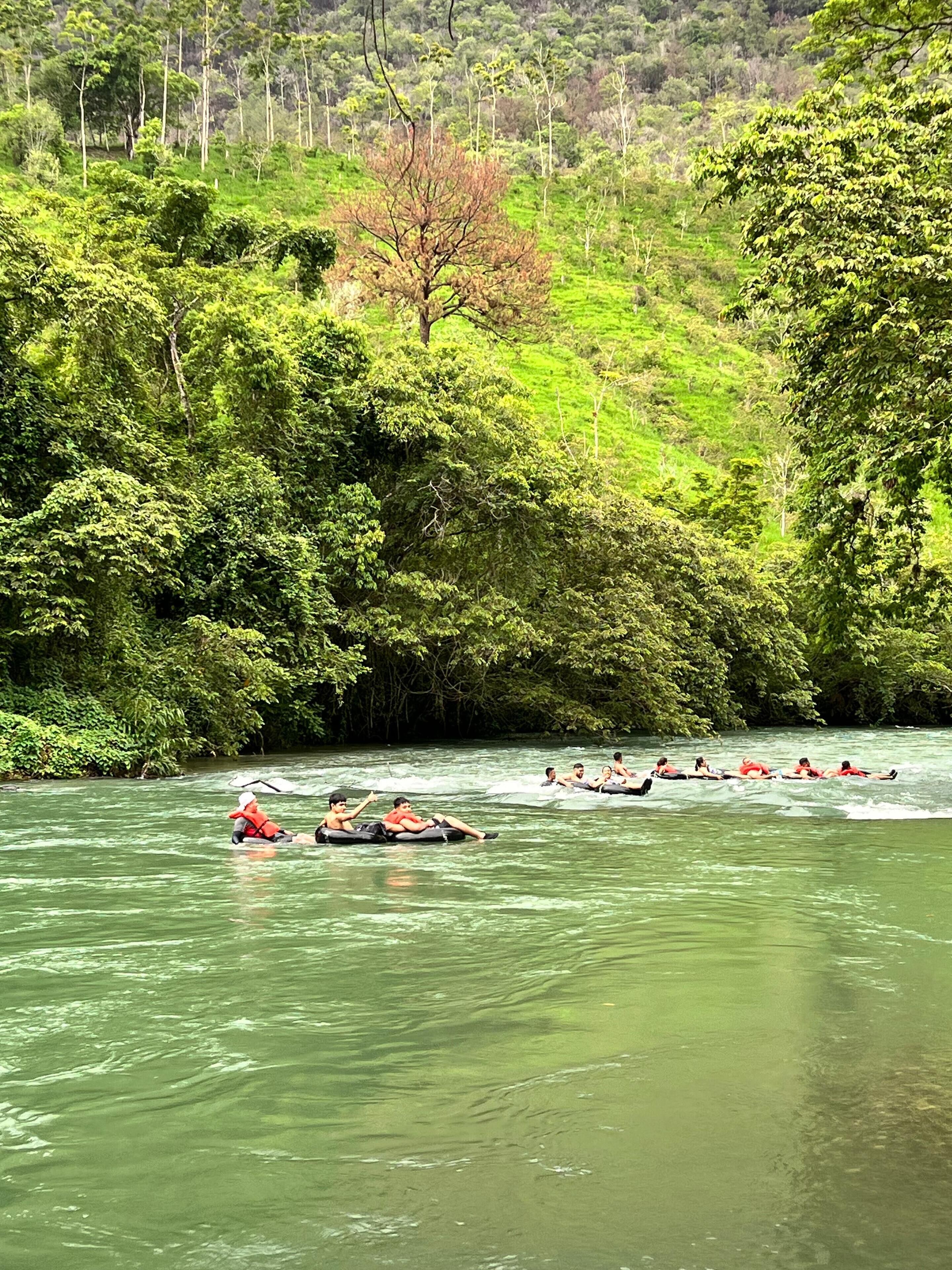 Un groupe de personnes fait du rafting sur une rivière bordée d’une végétation luxuriante.