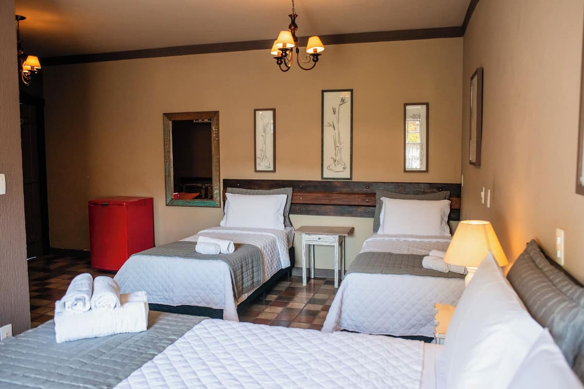 Quarto de hotel com duas camas, uma mesinha, um espelho e um candelabro.