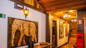 A hallway with a wooden ceiling, a large elephant sculpture on the wall, a vintage-style lamp, and a red fire alarm box. - Pousada Tiradentes Village (Tiradentes)