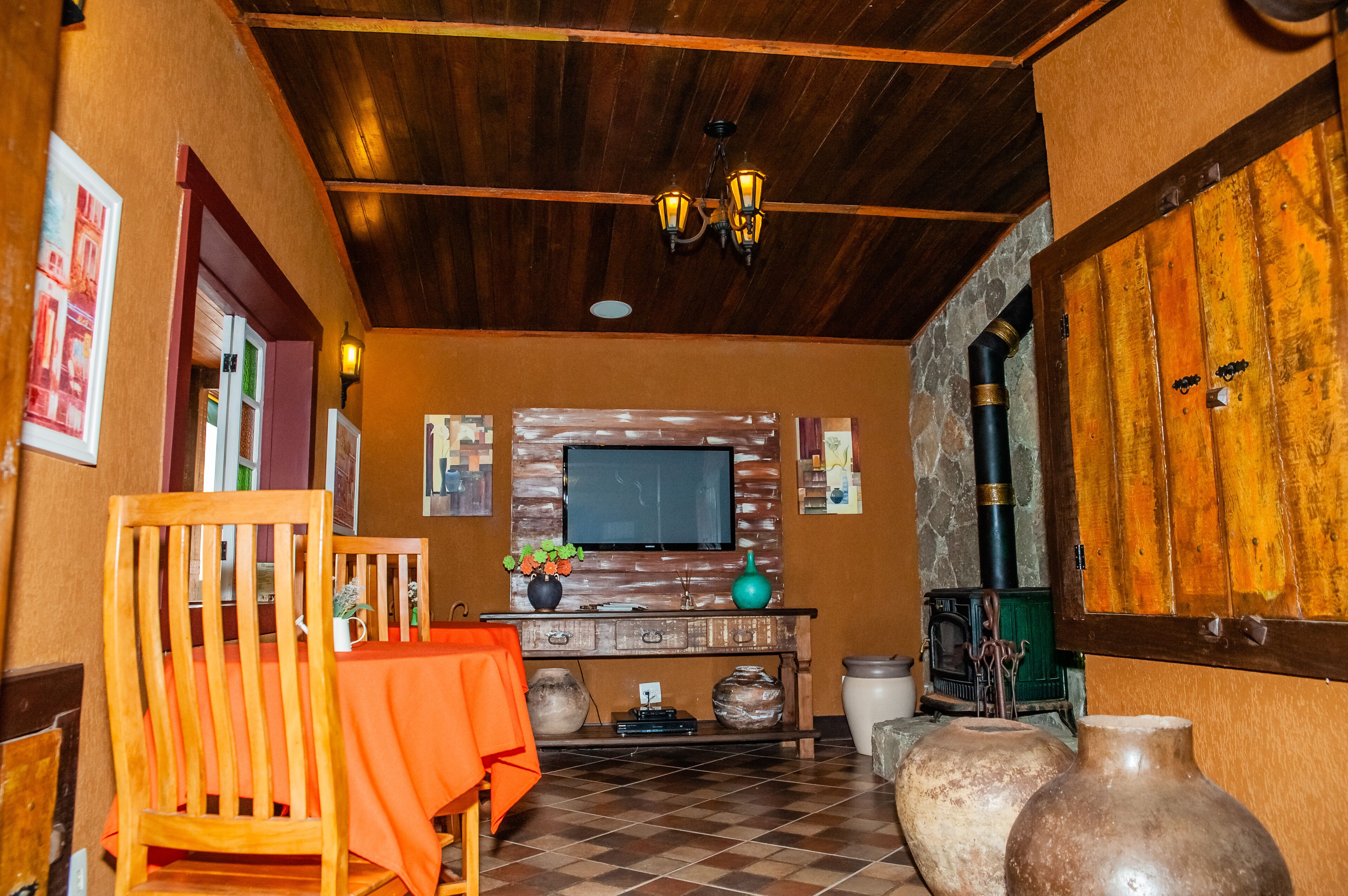 A cozy room with a wooden ceiling, a television mounted on a stone wall, a wooden cabinet, and a large vase.