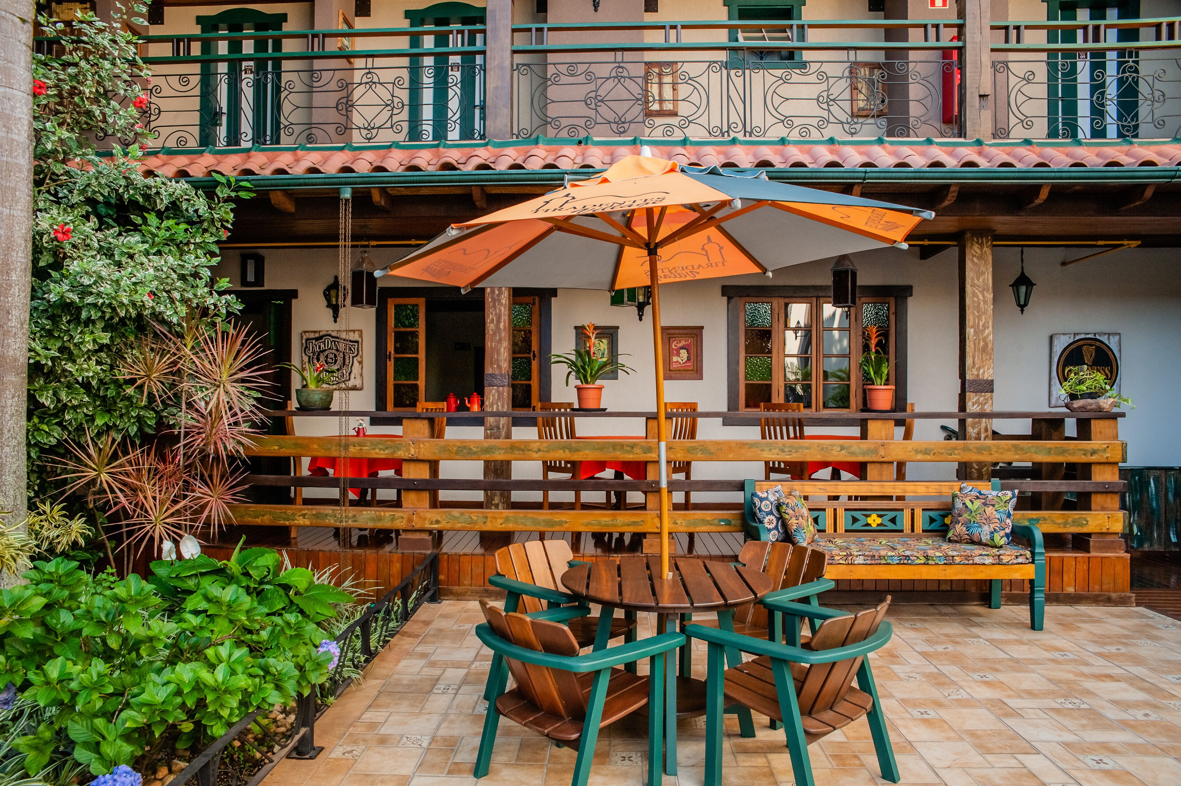 An outdoor patio with wooden tables and chairs, a large umbrella, and potted plants.
