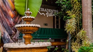 A tiered fountain with water cascading down, surrounded by lush greenery and a sign for 'Tiradentes Villa'. - Pousada Tiradentes Village (Tiradentes)