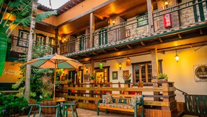 A multi-level outdoor seating area with wooden benches and tables, surrounded by potted plants and a large umbrella. - Pousada Tiradentes Village (Tiradentes)