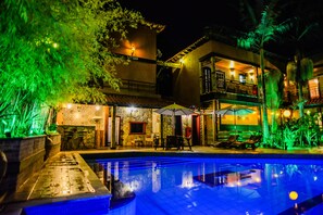 A nighttime view of a hotel with a swimming pool, outdoor seating, and a well-lit patio area. - Pousada Tiradentes Village (Tiradentes)
