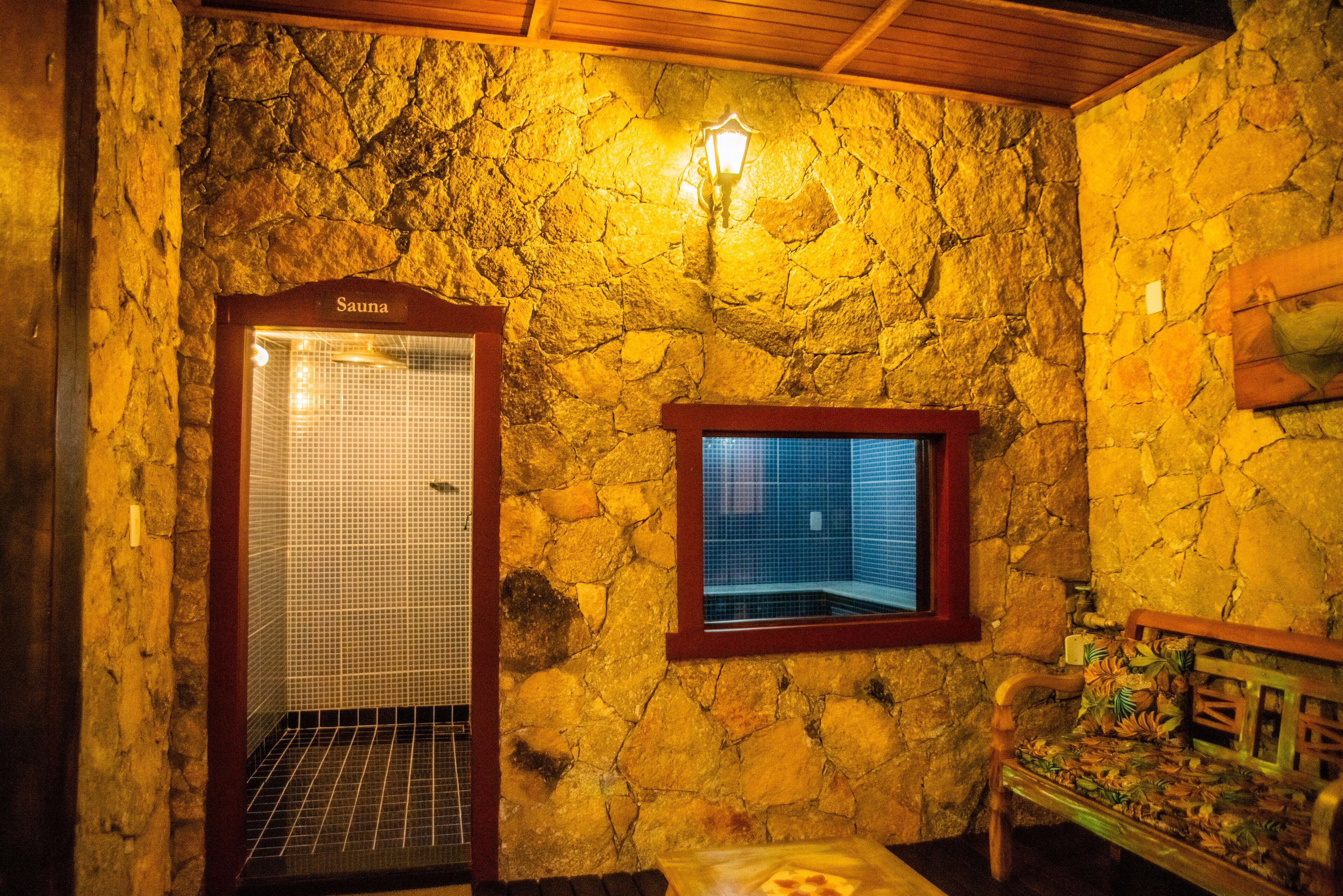 Um espaço sauna com paredes de pedra, um banco de madeira e uma pequena janela.