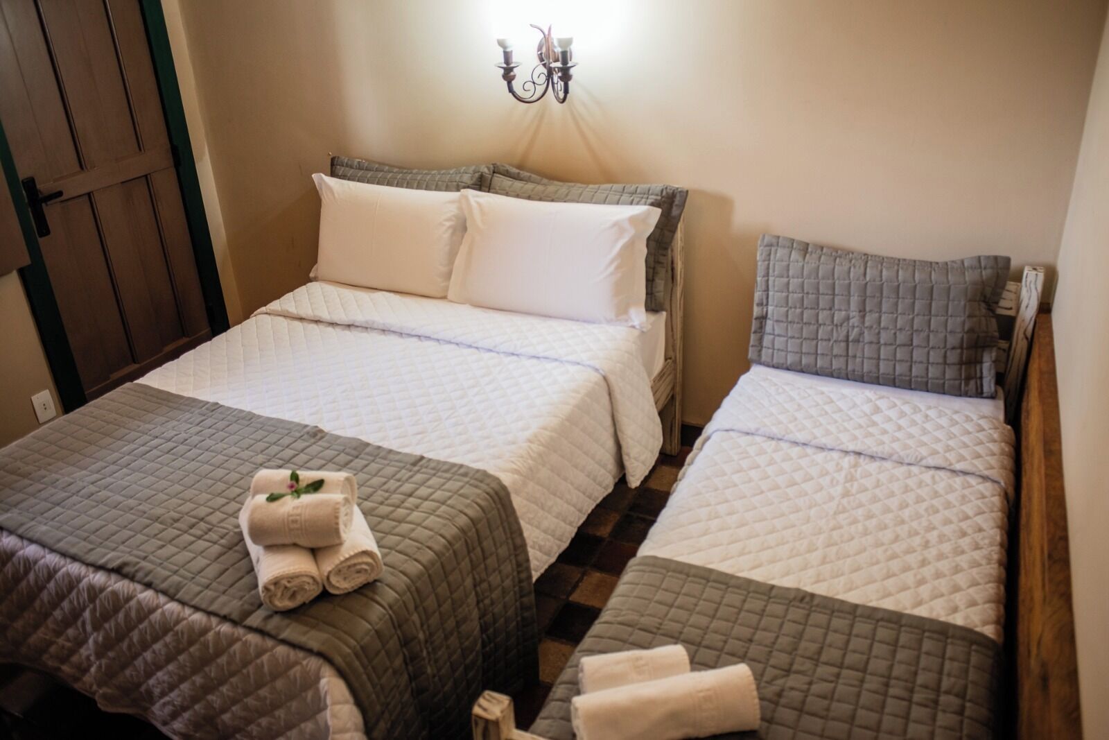 A hotel room with two beds, each with a quilted bedspread and pillows. There is a wall-mounted light fixture above the beds.