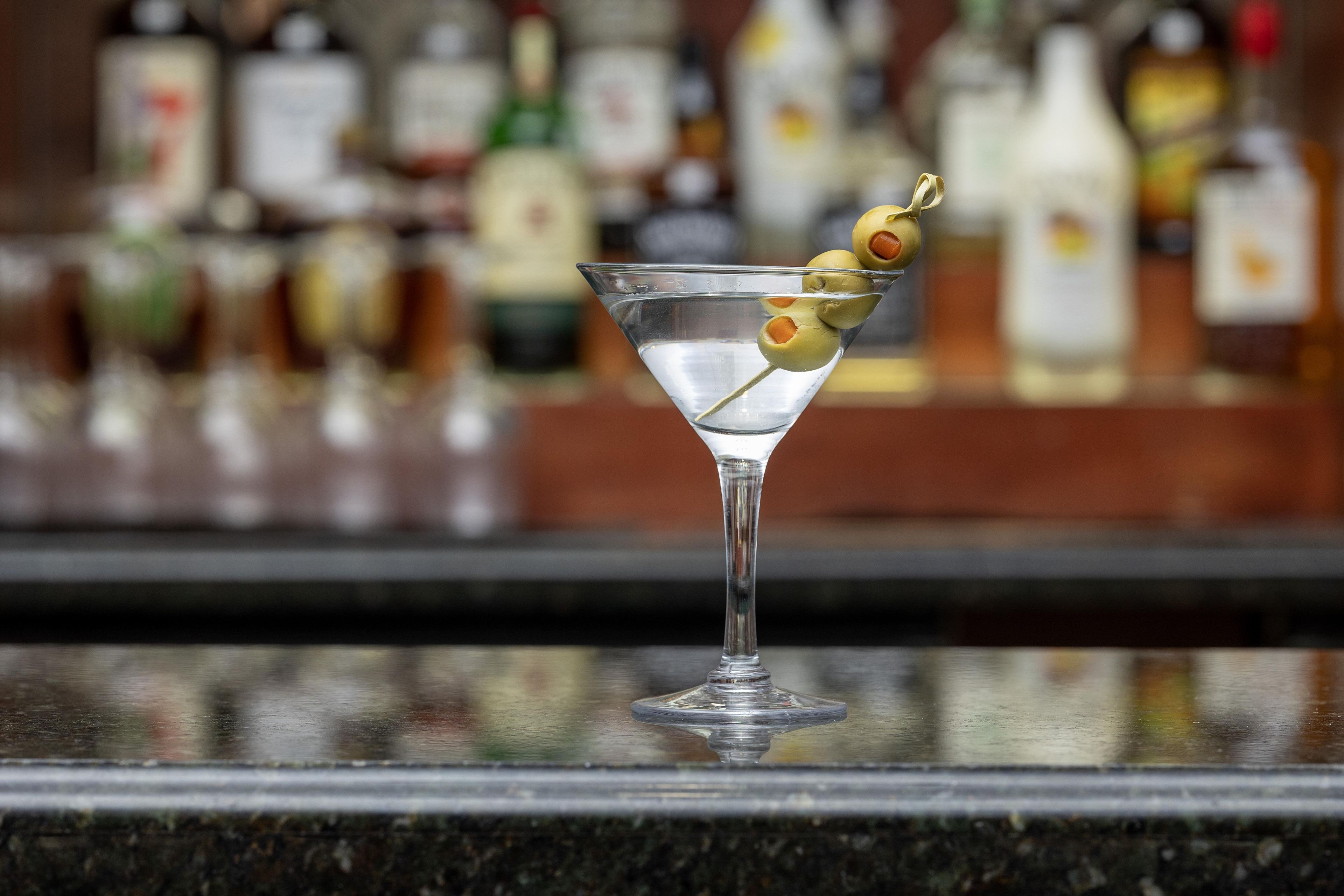 Una copa de martini con aceitunas sobre una barra.