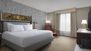 A hotel room with a large bed, a desk, a chair, a lamp, and a painting on the wall.