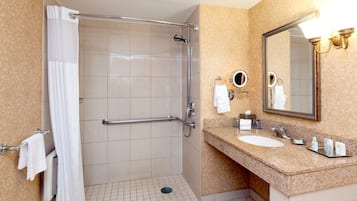 A hotel bathroom with a shower, a sink, a mirror, and towels.