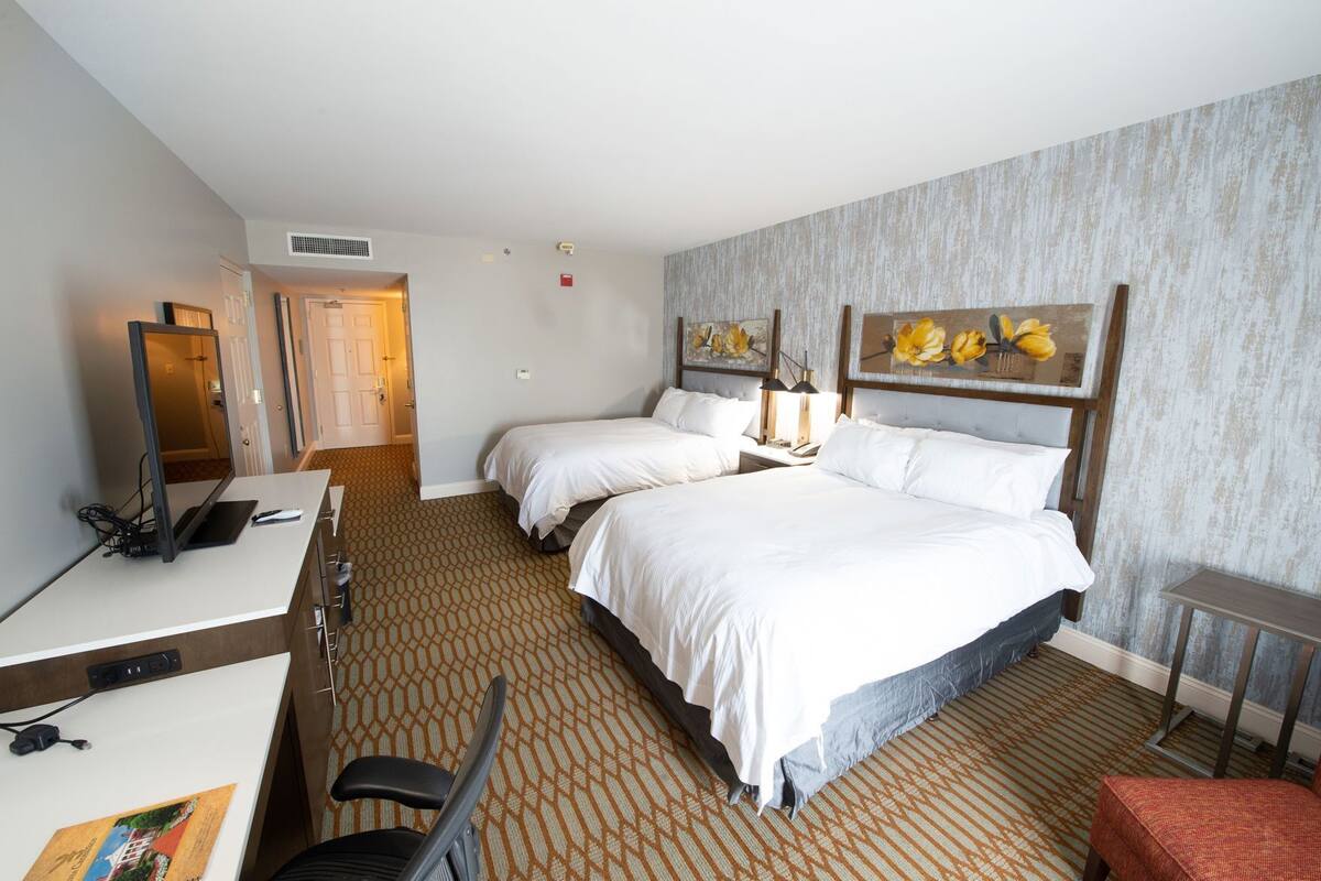 A hotel room with two beds, a desk with a computer, a chair, and a small table.