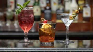 Drie cocktails op een bar met een wazige achtergrond van flessen.