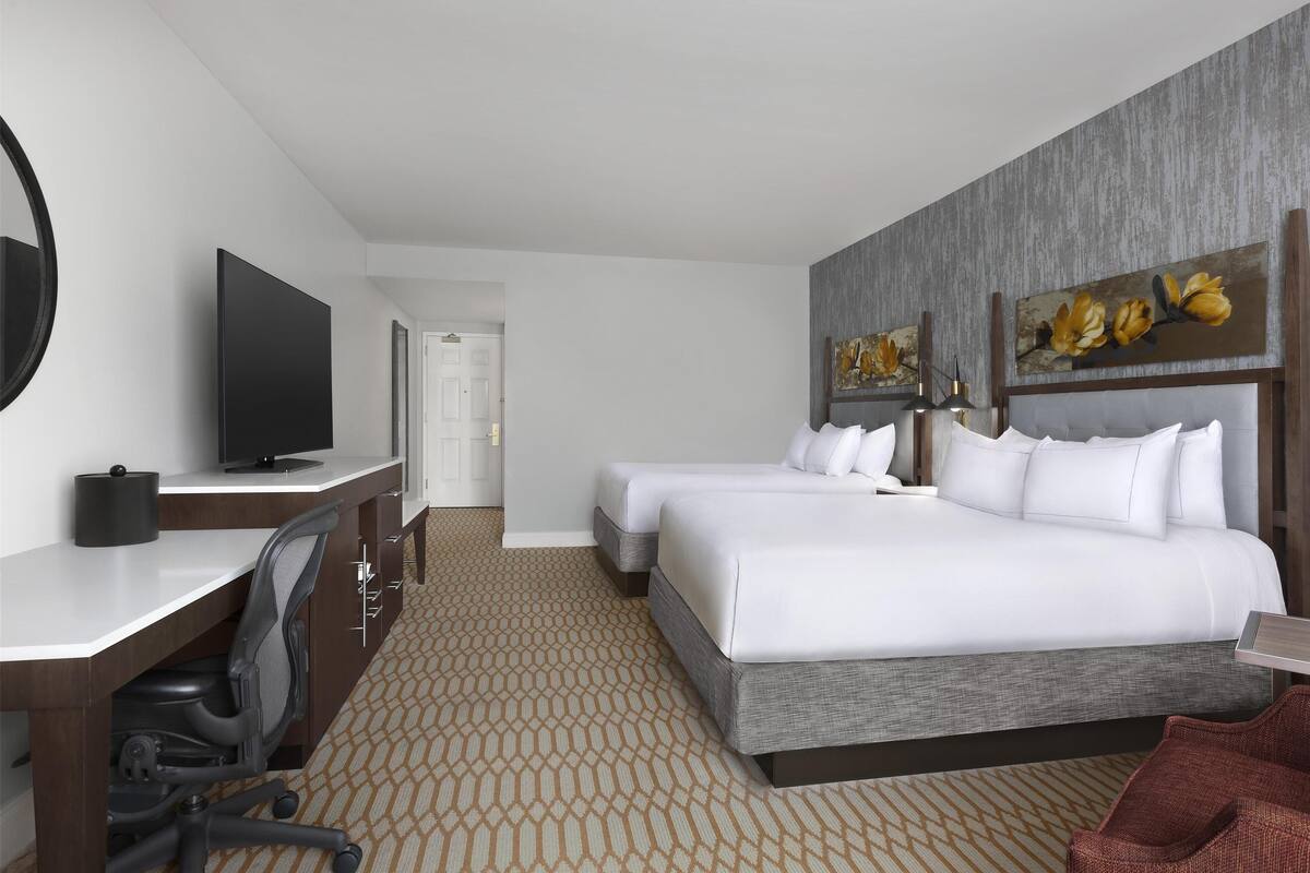 A hotel room with a large bed, a desk with a TV, a chair, and a red armchair.