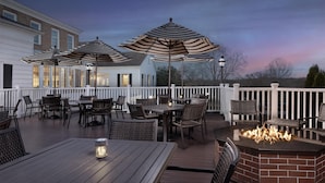 Une terrasse extérieure avec des tables et des chaises, des parasols à rayures et un foyer en briques.