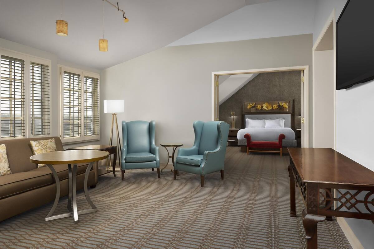 A hotel room with a sofa, two armchairs, a small round table, a bed, and a TV.
