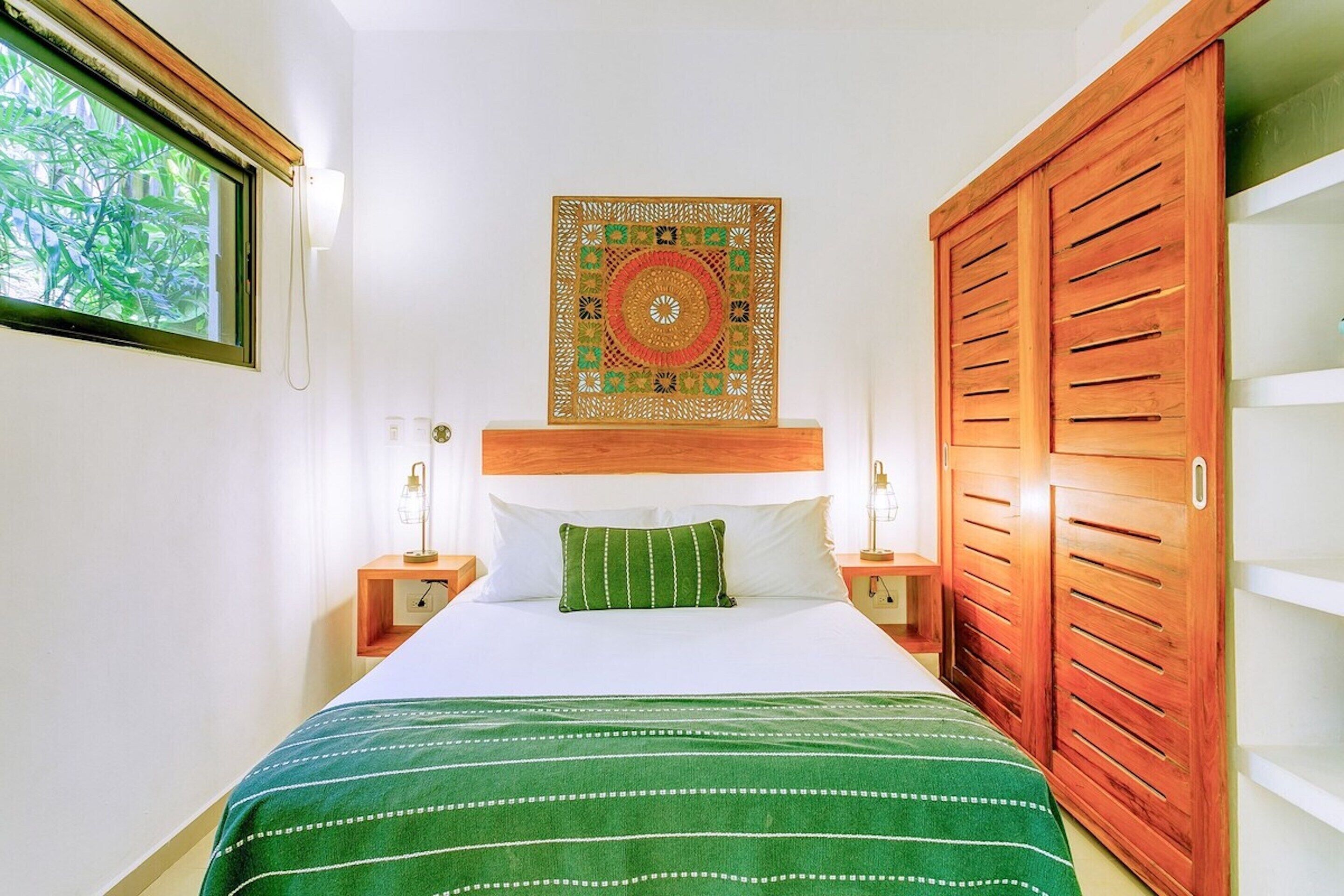 Una cama bien hecha con una colcha verde a rayas, un cabecero de madera y un adorno decorativo en la pared superior.
