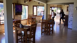 A spacious dining area with wooden tables and chairs, a television mounted on the wall, and a refrigerator with various stickers.